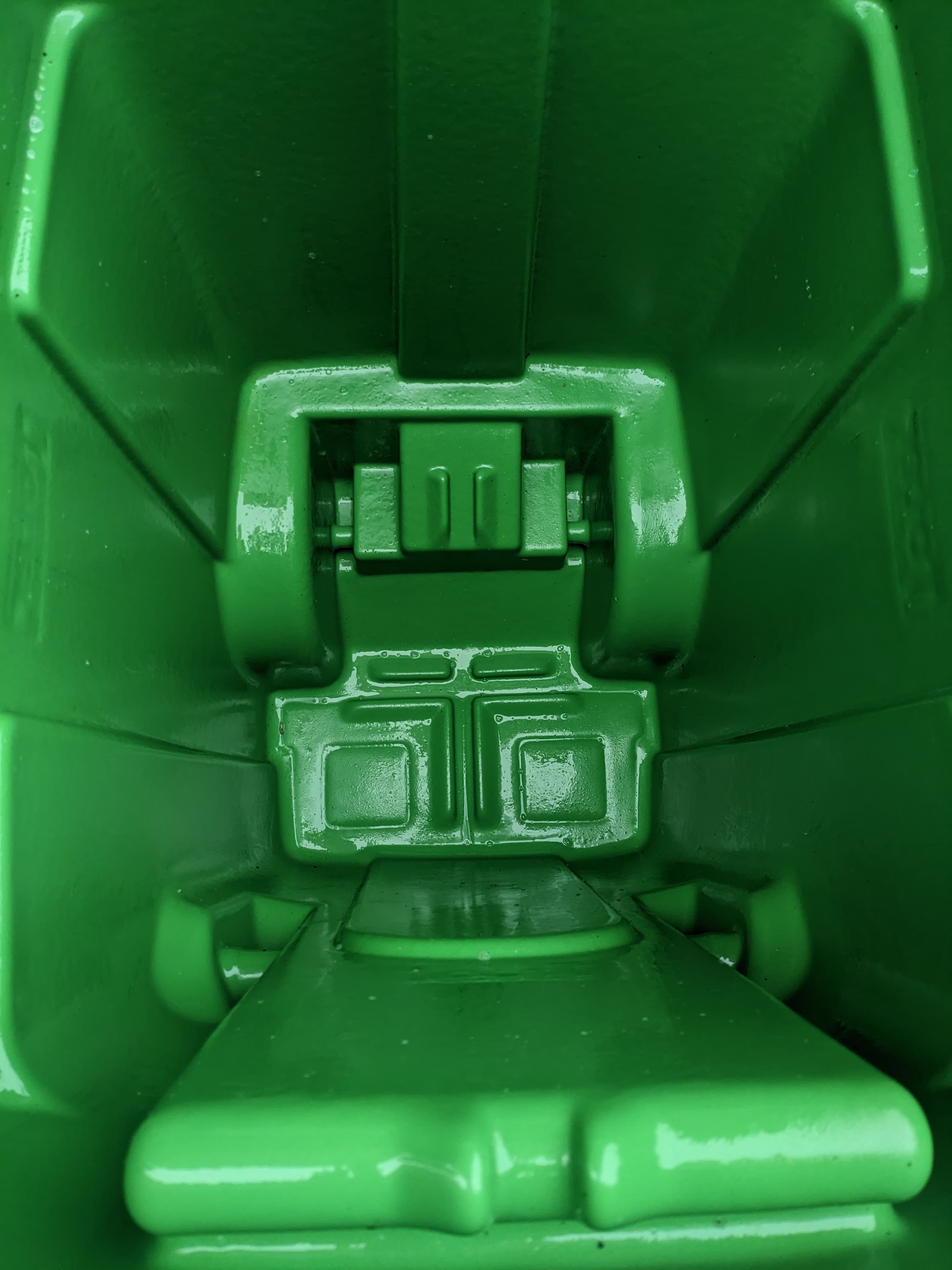 Top-down view into the empty, glossy green interior of a molded plastic waste container.
